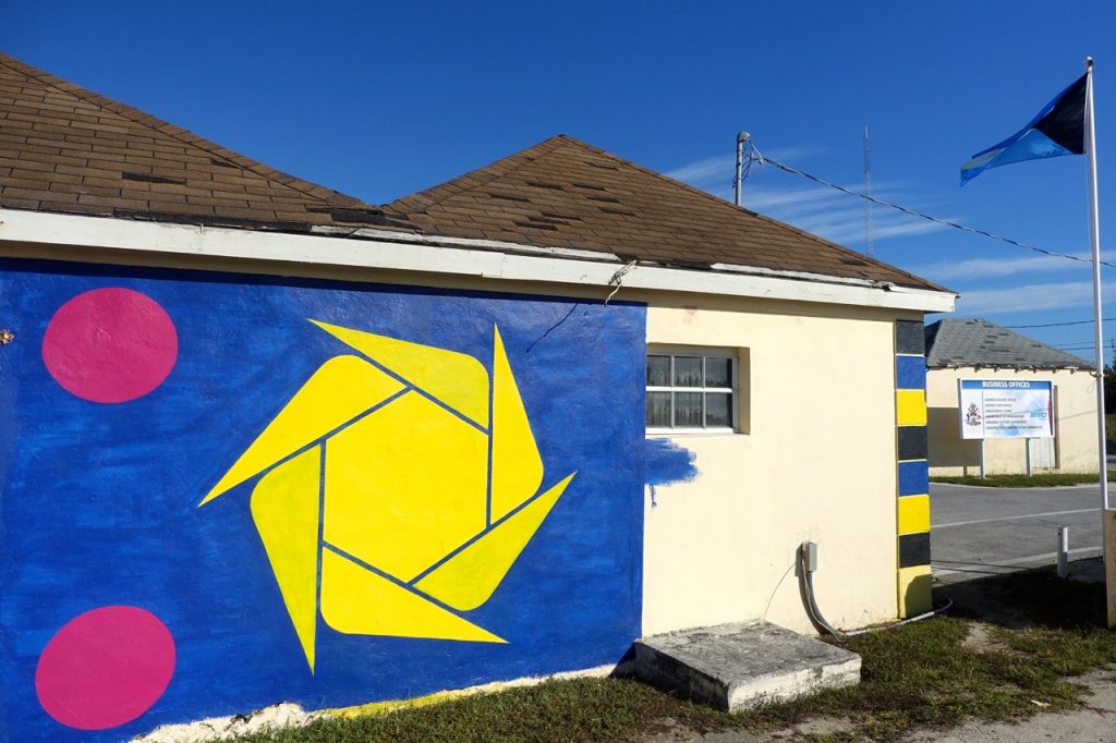 whilte 2 roofed building with a large mural showing the country flag on the side - yellow blue and pink