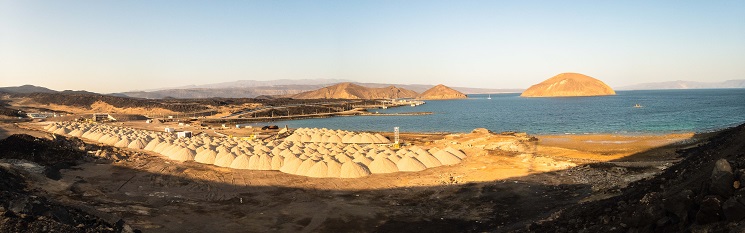 A sandy bay with sandy islands offshore and lining the bay small heaps of mined salt