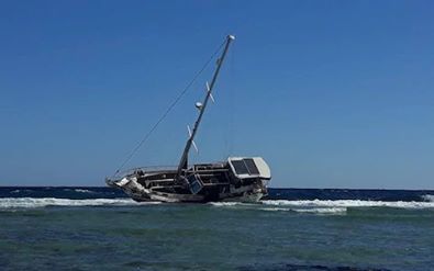 yacht with no sails and tall mast dry on a reef leaning over dramatically to port