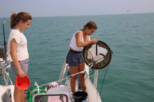 Two girls on board a yacht taking water samples